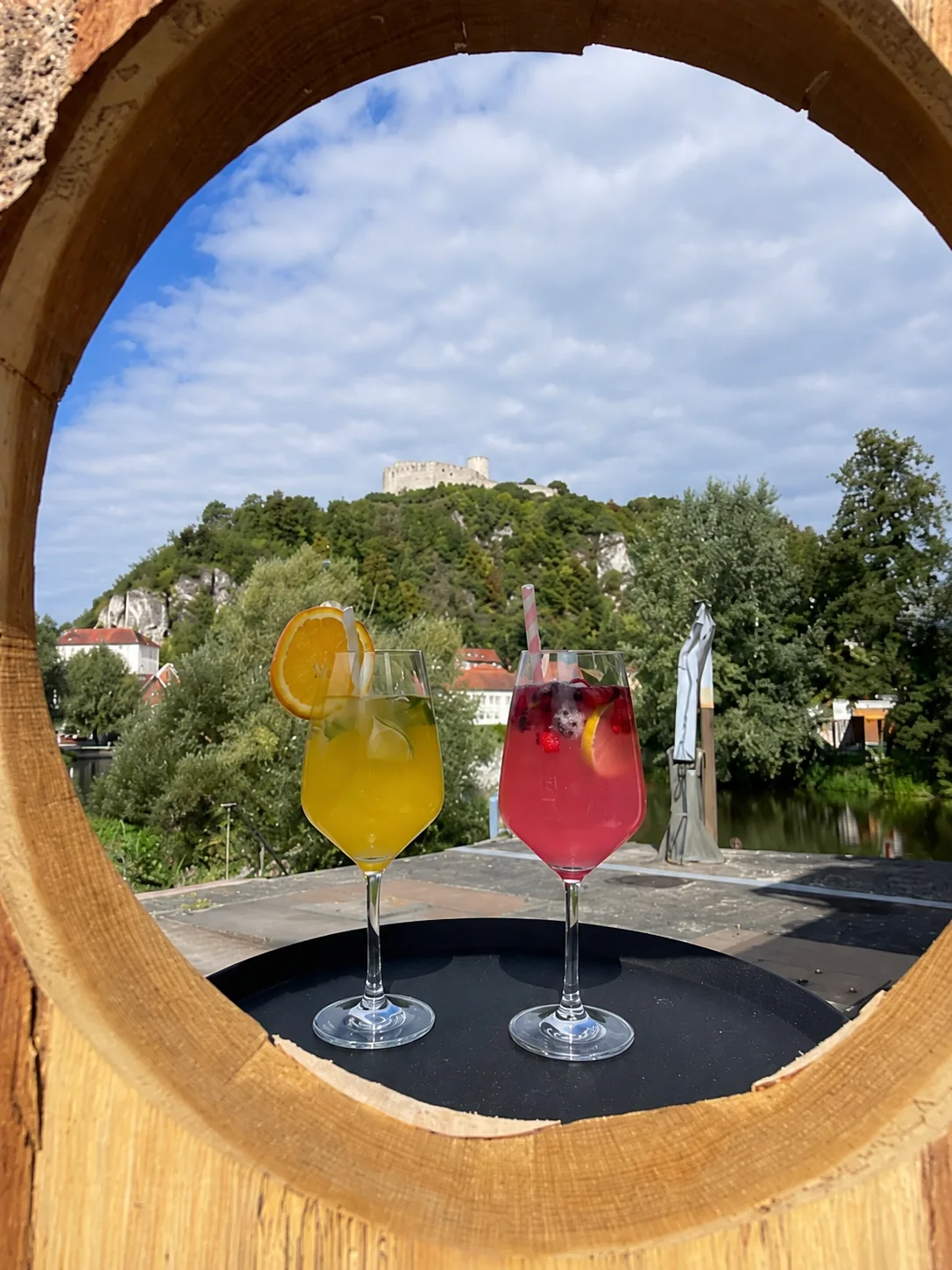Zwei Spritz-Cocktails, gerahmt vom runden Fass-Durchblick, dahinter die Burgruine und die Naab